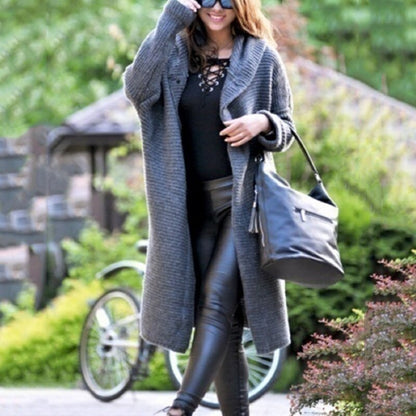 Eine Frau trägt eine lange graue Strickjacke mit Kapuze auf weißem Hintergrund